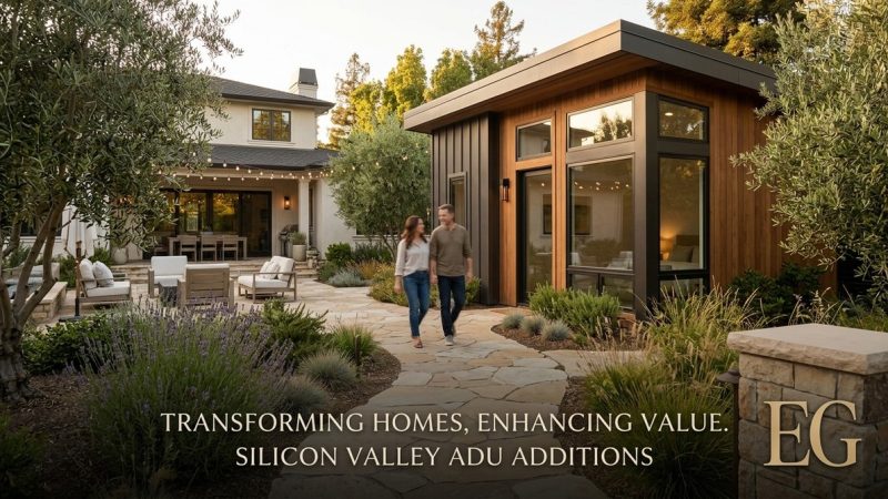 A couple walks on a stone path between a modern ADU and a large house with outdoor seating.
