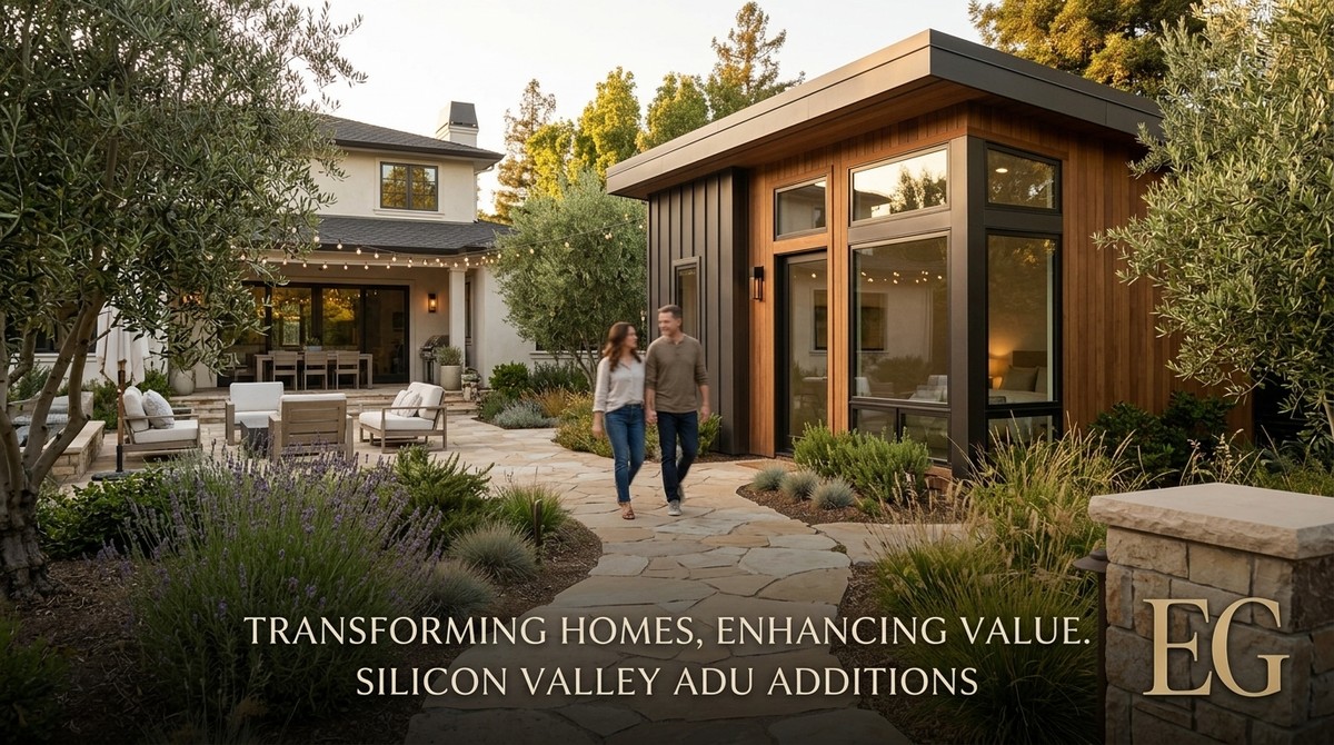 A couple walks on a stone path between a modern ADU and a large house with outdoor seating.