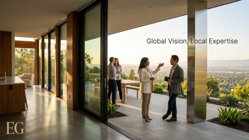Four people converse on a modern patio overlooking a lush, green Bay Area landscape at sunset.