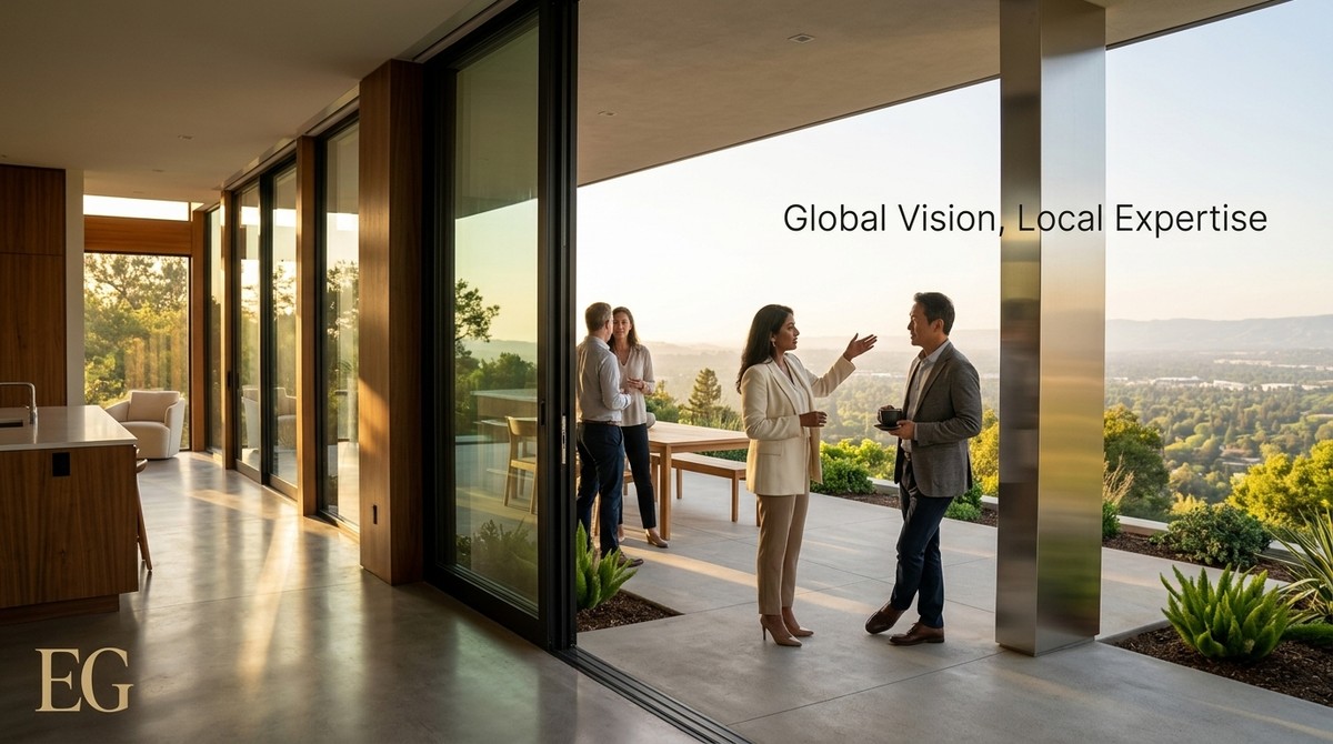 Four people converse on a modern patio overlooking a lush, green Bay Area landscape at sunset.